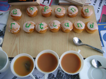 cakes spelling expandrutland and 3 cups of tea on table